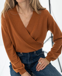 Woman wearing a PLEIN PUBLIQUE wrap sweater LES CINQ Terra, seated against a light background.