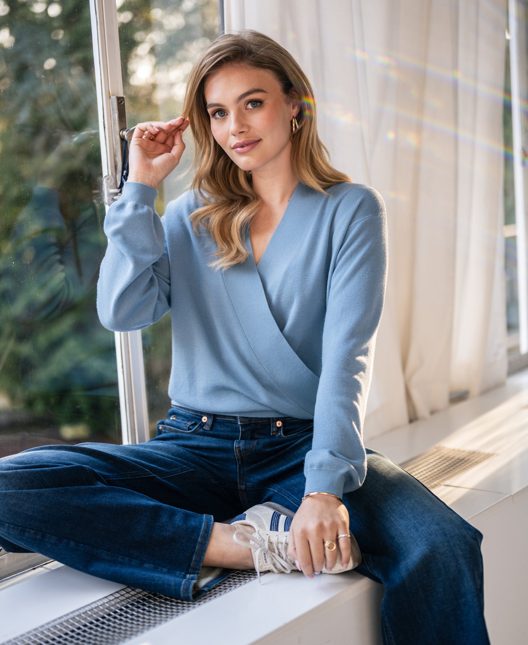 Woman wearing the LES CINQ cross-over sweater in denim blue from PLEIN PUBLIQUE.