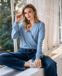 Woman wearing the LES CINQ cross-over sweater in denim blue from PLEIN PUBLIQUE.