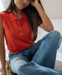 Sleeveless coral knit polo top by Plein Publique, shown on a model with long brown hair over one shoulder.