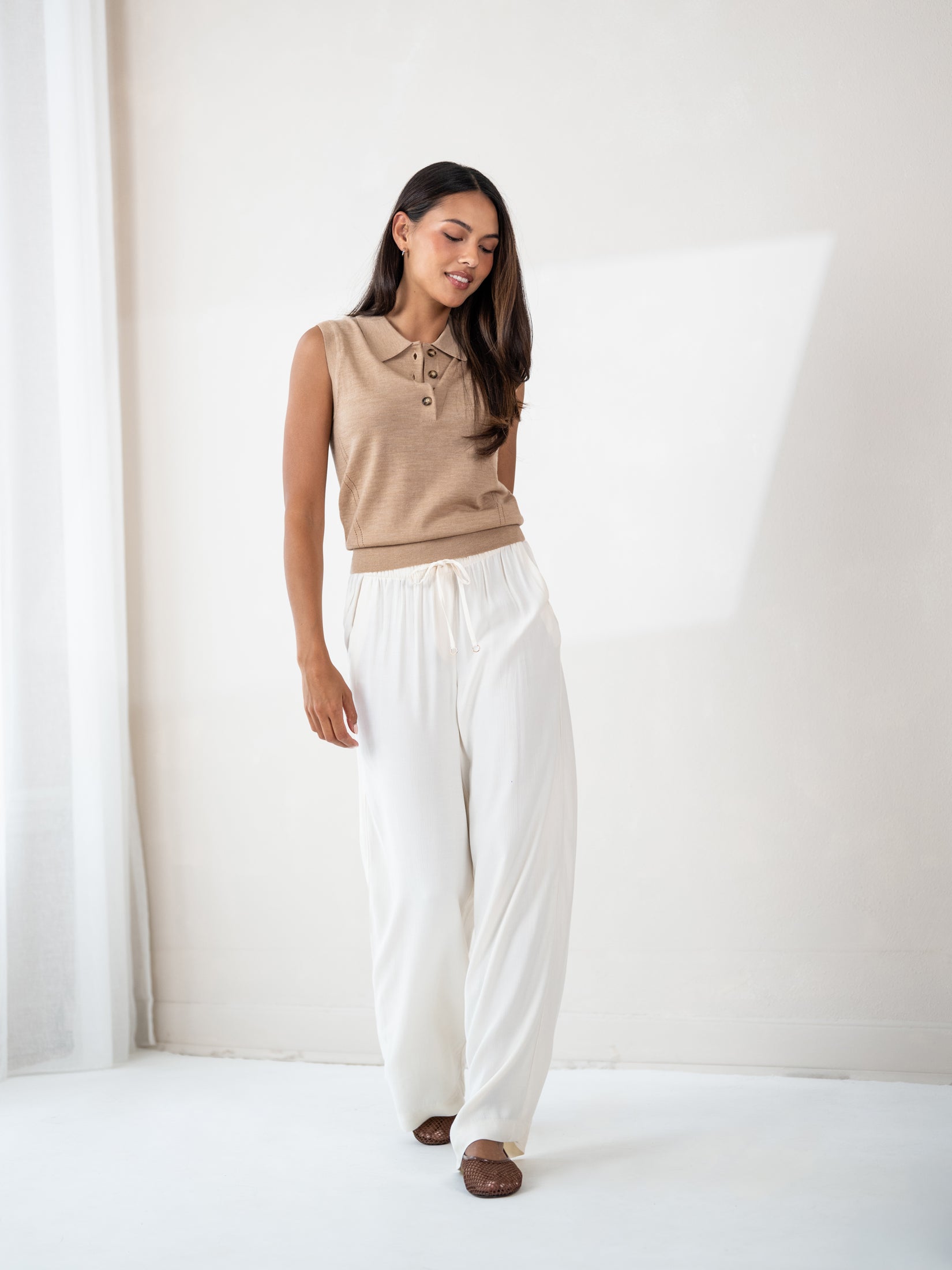 Sleeveless polo sweater in soft camel by PLEIN PUBLIQUE, shown in a bright, minimalist room.