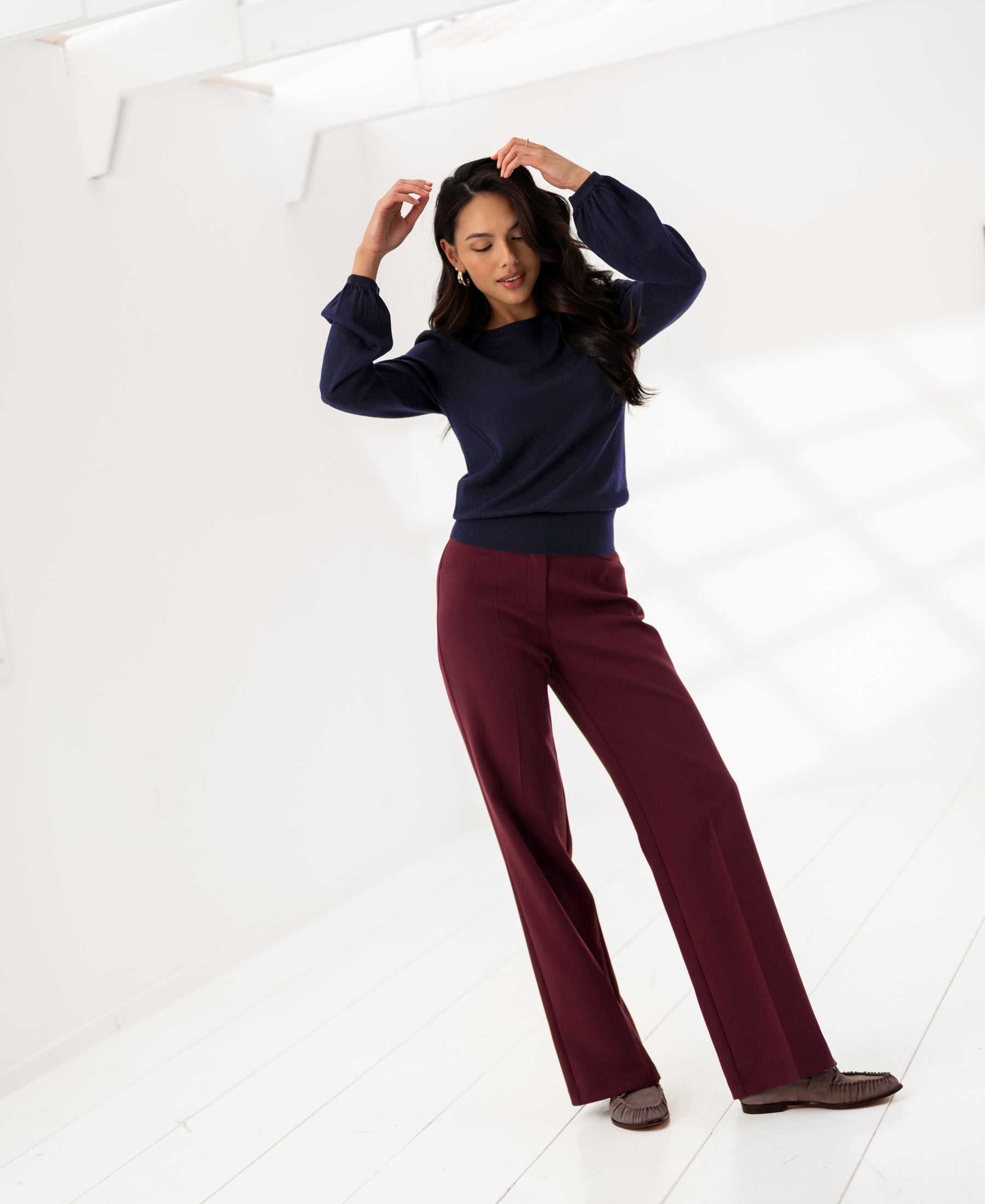 Woman indoors wearing PLEIN PUBLIQUE flexible trousers LA JOELLE Wine color, on a white floor with sunlight.
