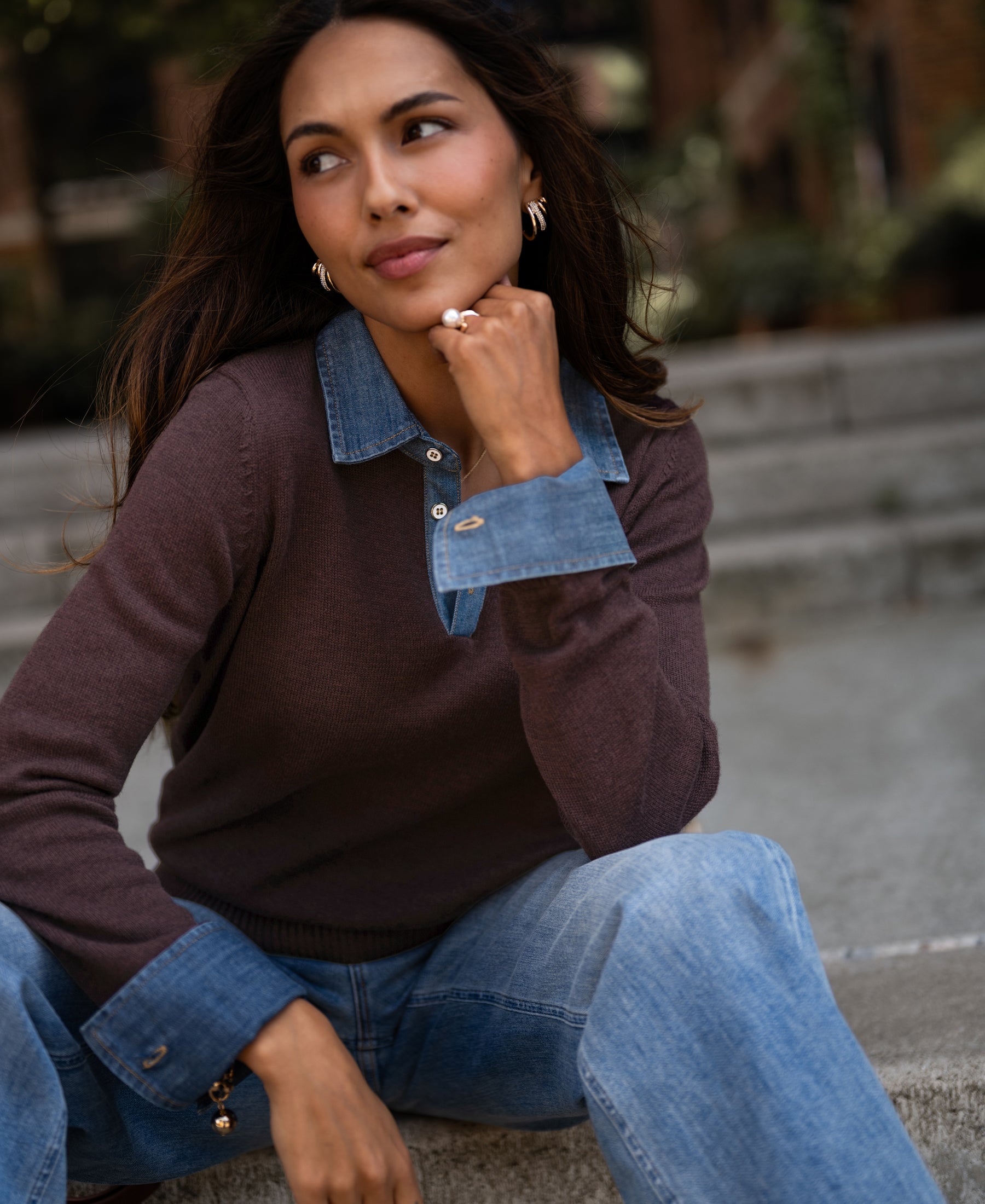 Woman wearing a brown knit pullover blouse, seated on outdoor steps.