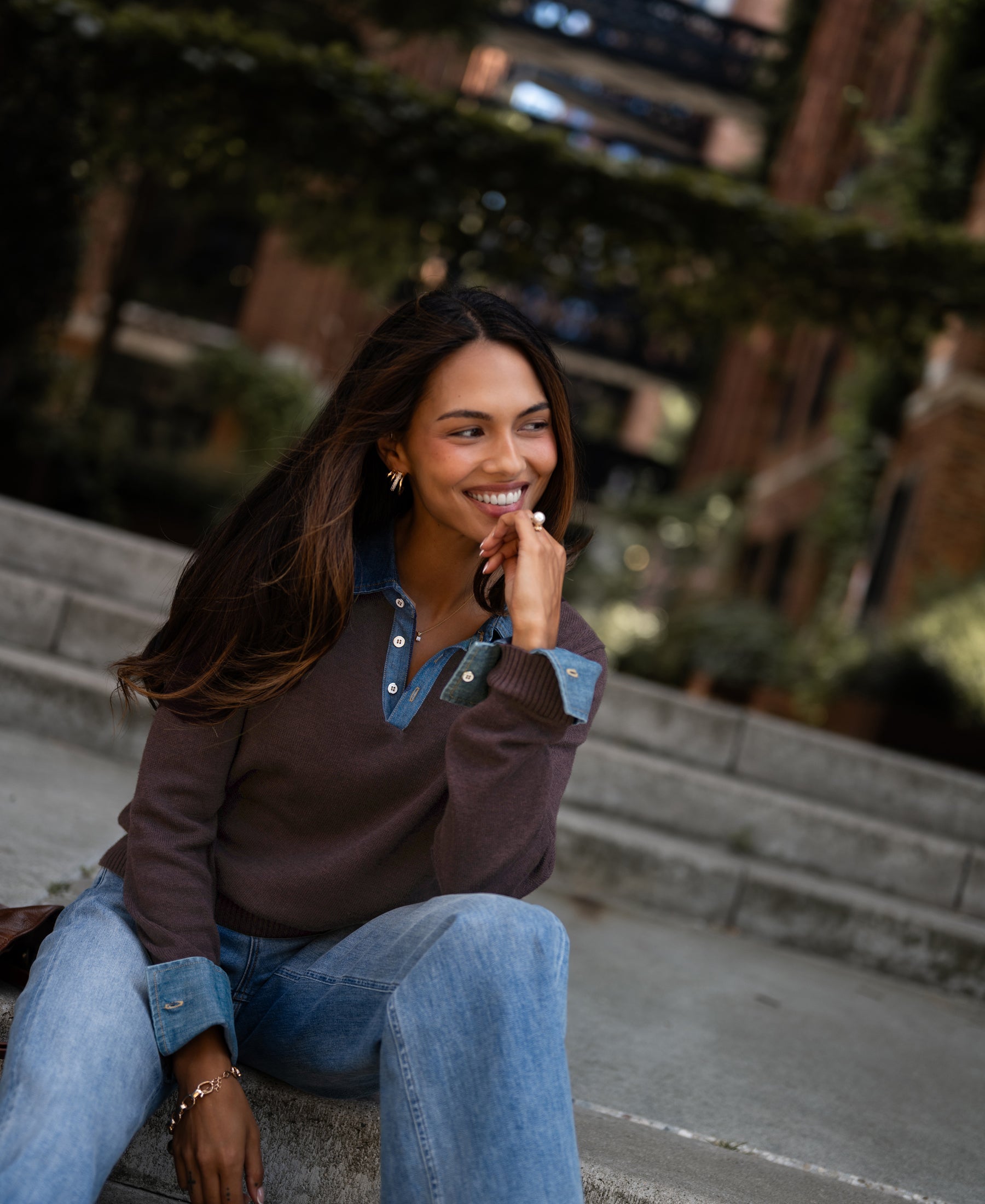 A woman with long hair outside, wearing the LA COLLEGE Pure choco sweater-blouse.