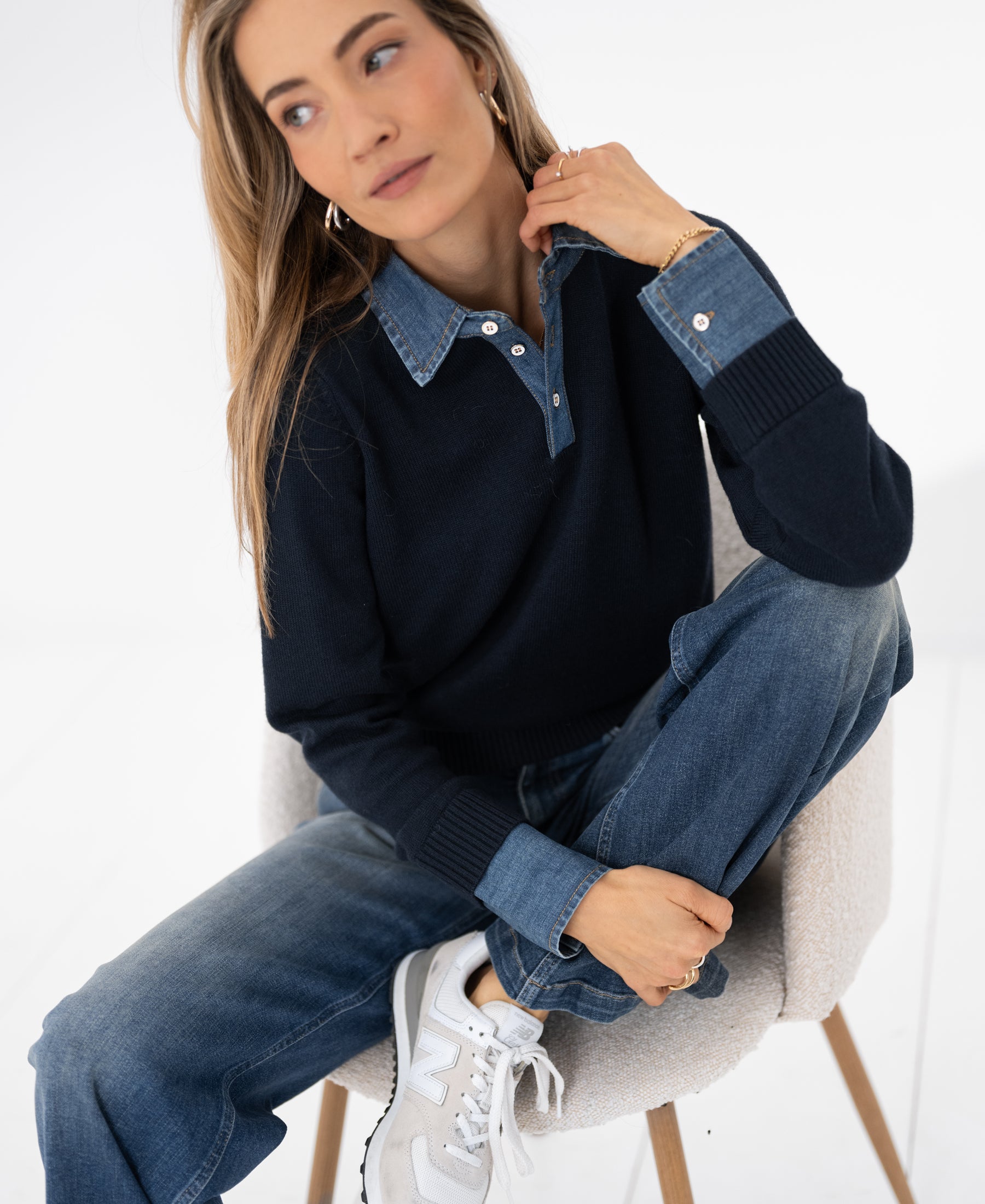 Dark blue sweater-blouse by PLEIN PUBLIQUE, shown on a seated model looking to the side.