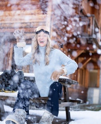 Vrouw draagt lichtblauwe LA COZY turtleneck sweater van PLEIN PUBLIQUE, buiten bij houten cabin.