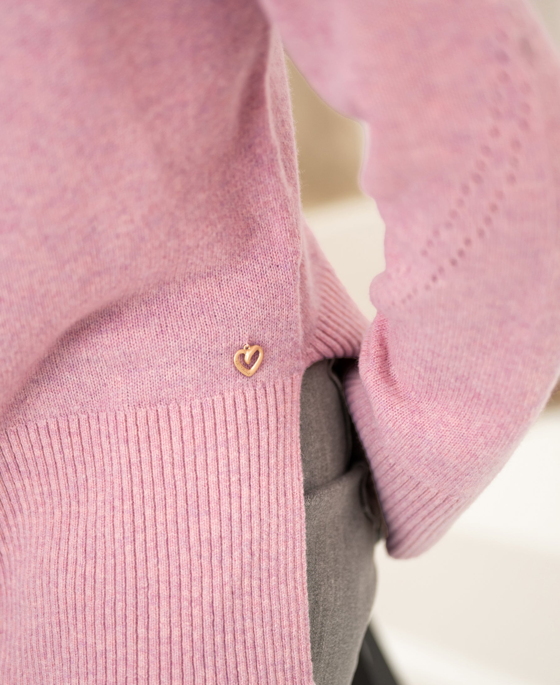Close-up of a person wearing a pink PLEIN PUBLIQUE LA COZY turtleneck with a small gold heart charm near the hem.