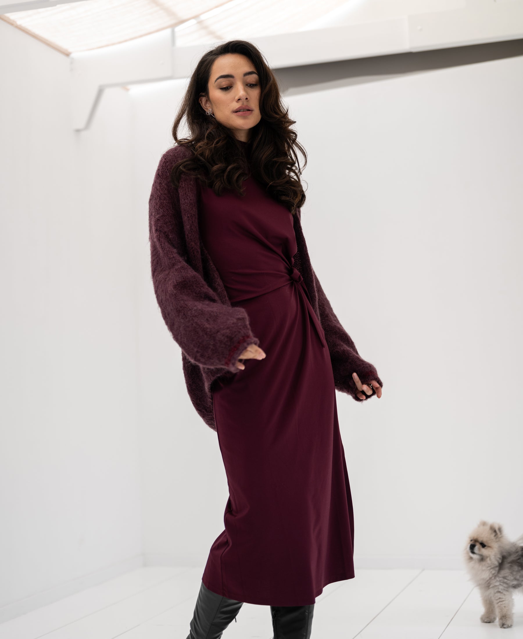 Woman wears Bordeaux fluffy vest; small fluffy dog sits nearby indoors.