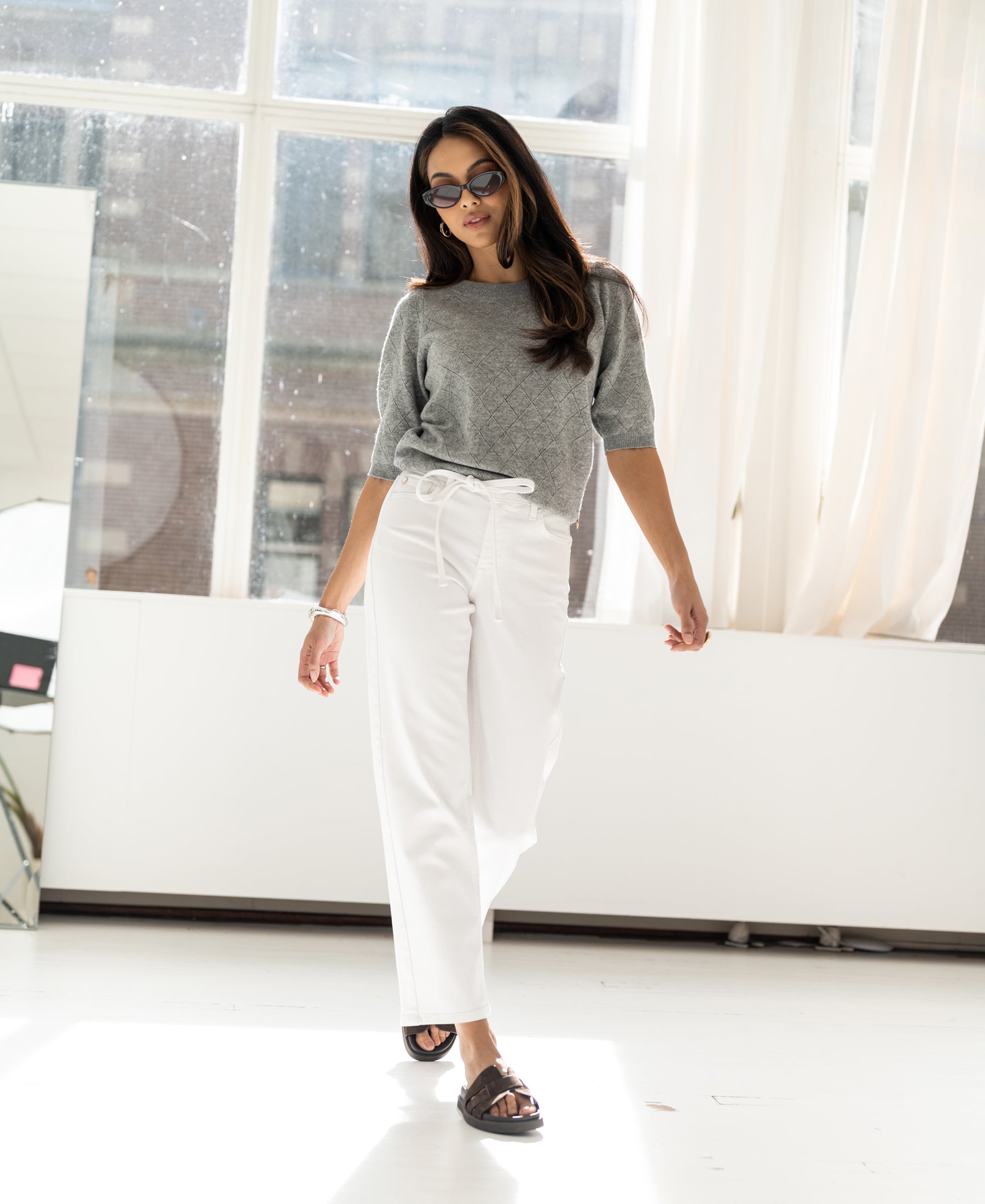 Cropped jeans, light wash, worn by a woman walking in a bright studio.