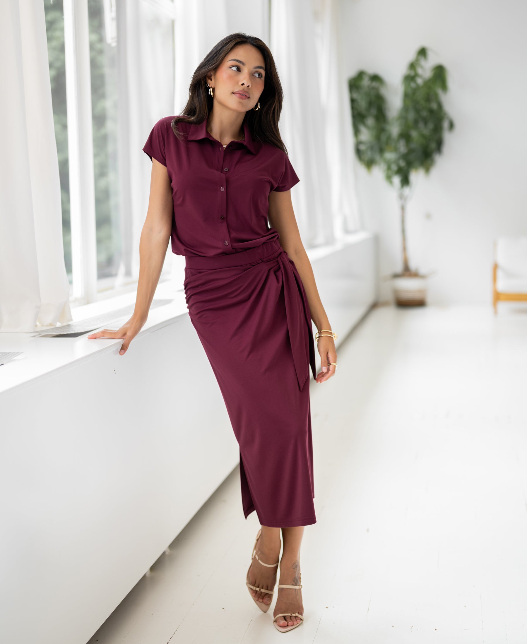 Wine-colored travel blouse in a bright, minimalist room.