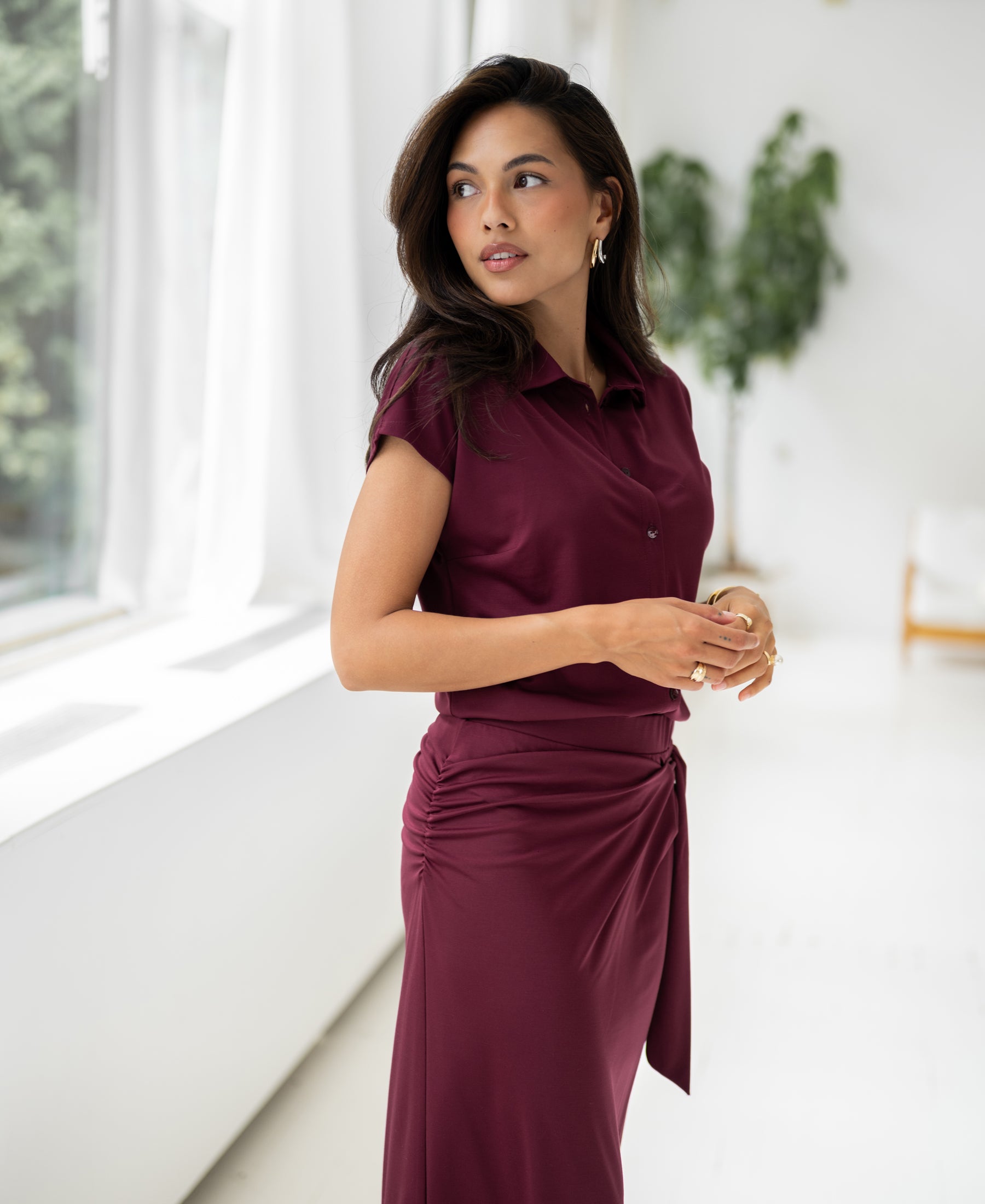 Wine-colored travel blouse in a front view, shown with one hand on the waist.