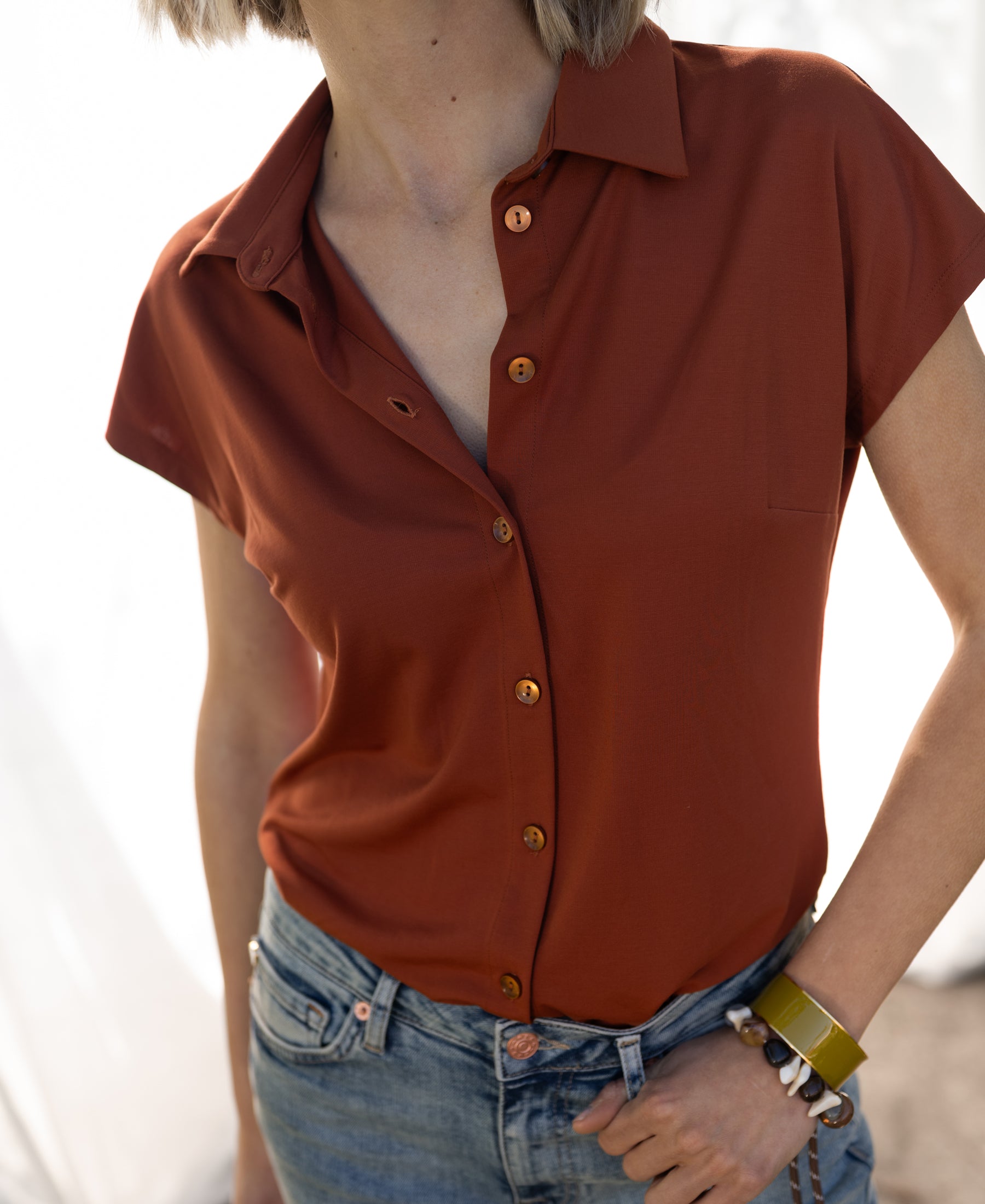 Woman wearing the PLEIN PUBLIQUE terra-colored travel blouse LA DELON stands outdoors.