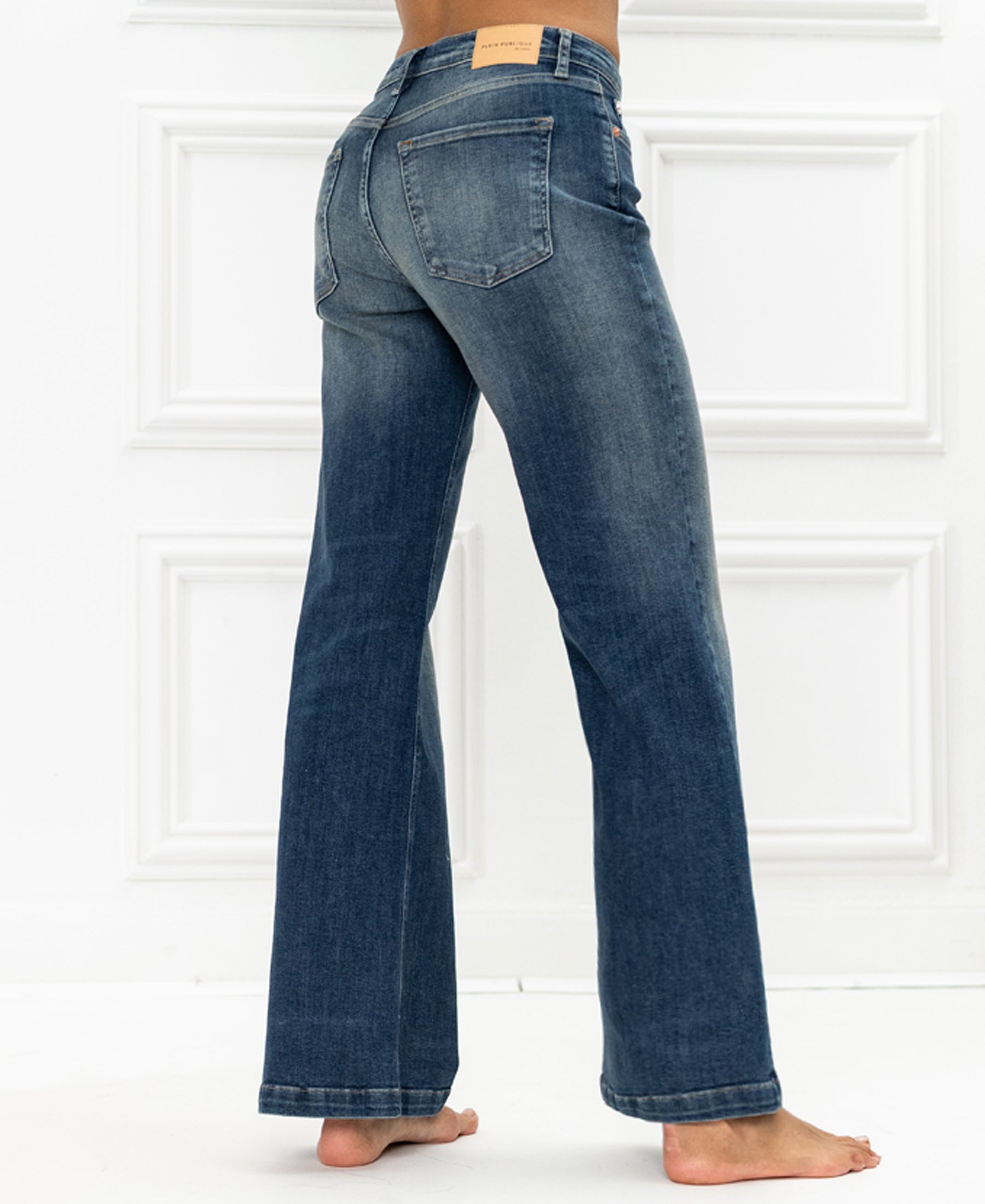 Wide leg blue vintage jeans by Plein Publique, shown on a person standing on a white floor with a panel wall background.