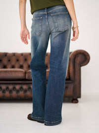 Person wearing blue wide leg jeans stands by a brown leather sofa on a white floor.