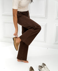 Person puts on tan leather loafers; white loafers and another shoe are nearby.