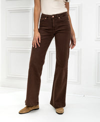 Woman wearing brown LES DEUX Cacao jeans in a white room with paneled walls.