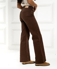 Woman wearing LES DEUX Cacao jeans stands by a white paneled wall.