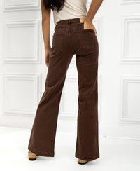 Woman wearing cacao-colored LES DEUX jeans stands by a white paneled wall.