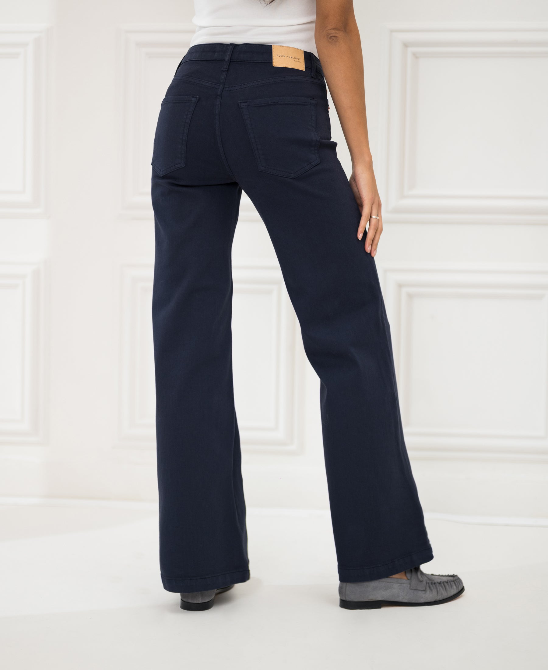 A person wearing dark blue LES DEUX jeans stands turned away in a white paneled room.