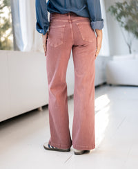 Dusty pink wide leg jeans by Plein Publique, shown indoors with sunlight streaming in.