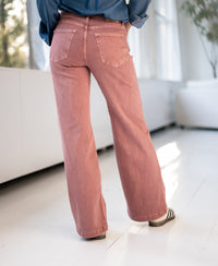 Person wearing dusty pink PLEIN PUBLIQUE LES DEUX jeans, standing indoors by large windows.