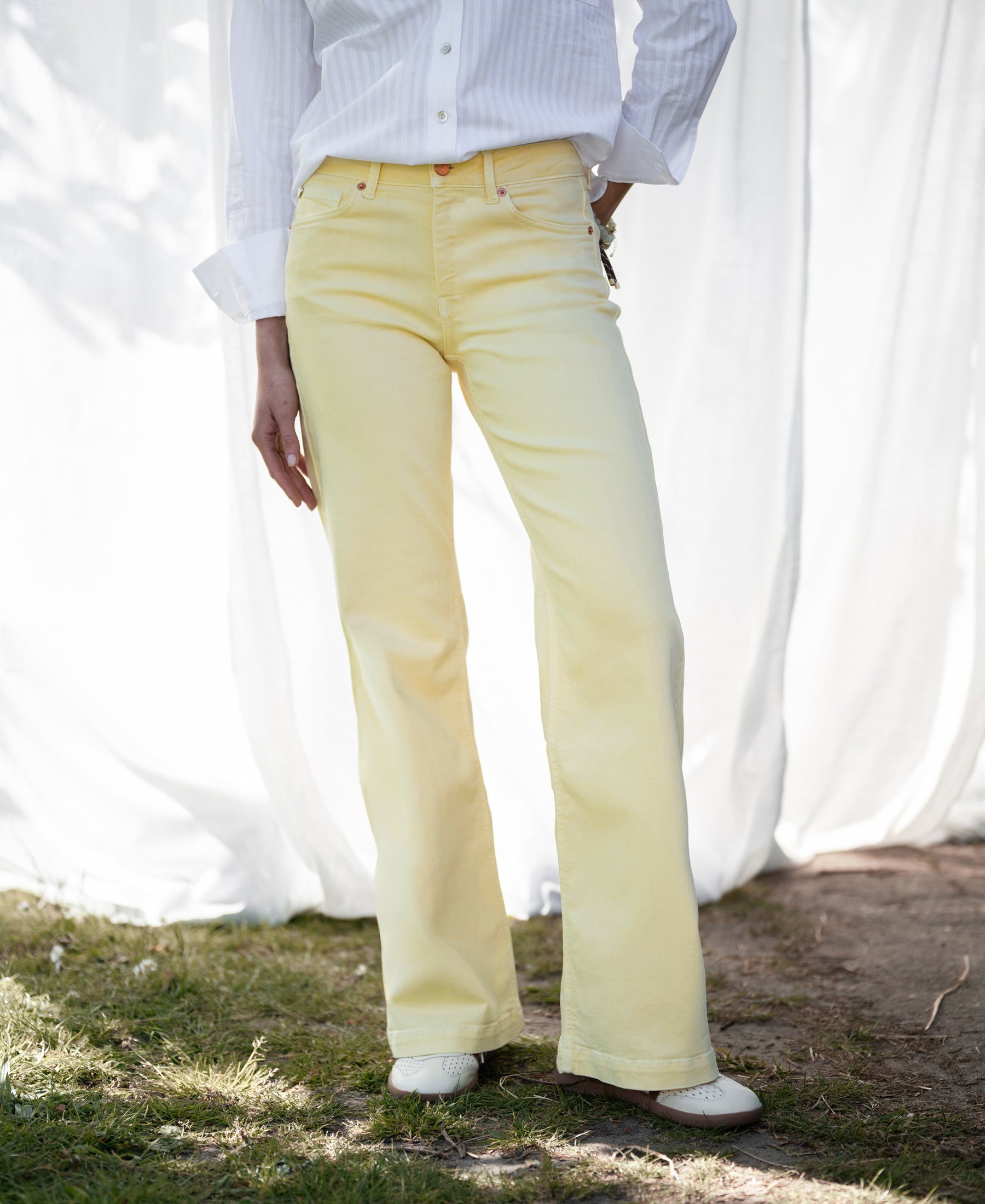 Wide leg jeans in soft yellow shown outdoors with a curtain backdrop.