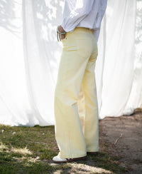 Person wearing wide leg jeans in soft yellow outdoors on grass with a white curtain backdrop.
