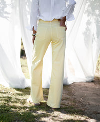 Person outdoors wearing wide leg jeans in soft yellow by Plein Publique, with white curtains in the background.