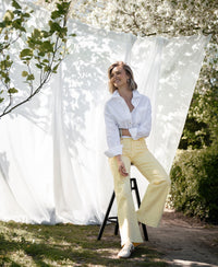 Wide leg jeans in soft yellow are worn by a person sitting outdoors under white fabric.