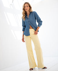 Wide leg yellow jeans shown on a model, facing the camera in a bright white room.