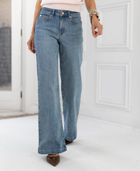 Wide leg jeans in light stone color from Les Deux, shown worn by a person standing indoors by a white door.