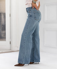 Wide leg jeans in light stone color shown from the side in a bright, minimal room.