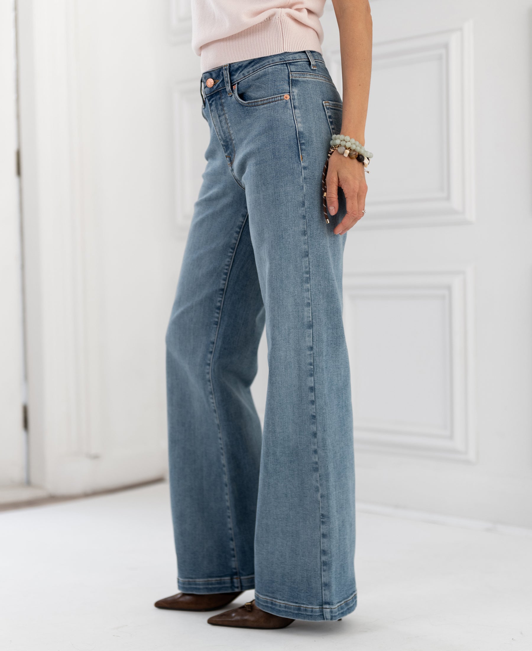 Wide leg jeans in light stone color, shown on a person standing on a white indoor floor.