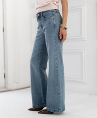 Wide leg jeans in light stone color, shown on a person standing on a white indoor floor.