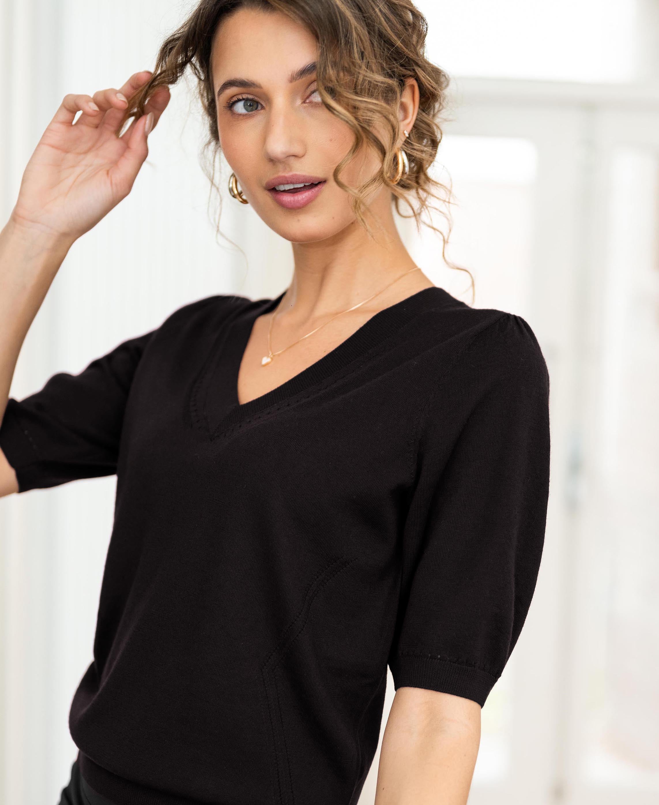 Woman wears black PLEIN PUBLIQUE LA DIAZ V-neck sweater, standing indoors.