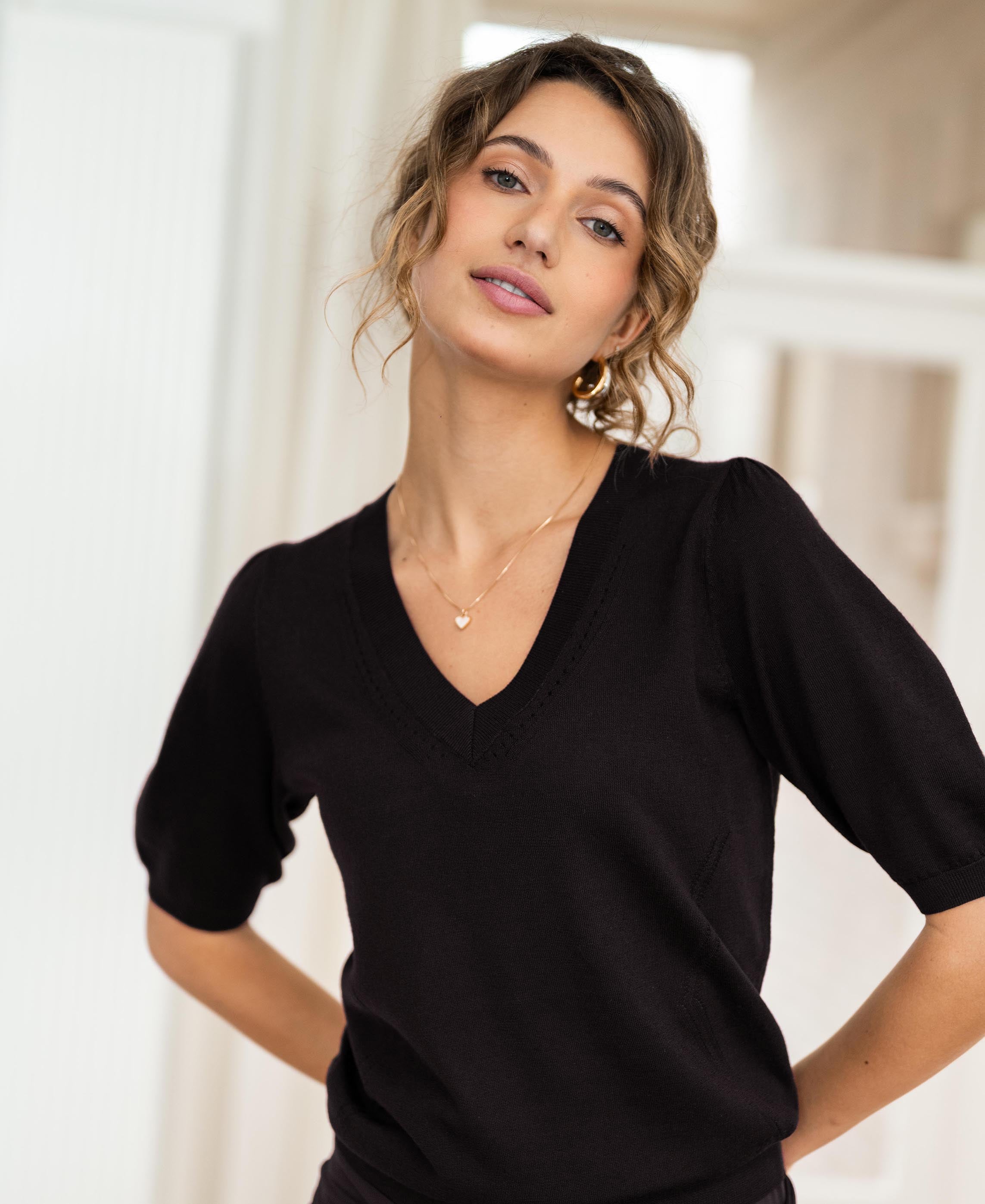 Black V-neck sweater in soft knit, shown on a person indoors with a blurred background.
