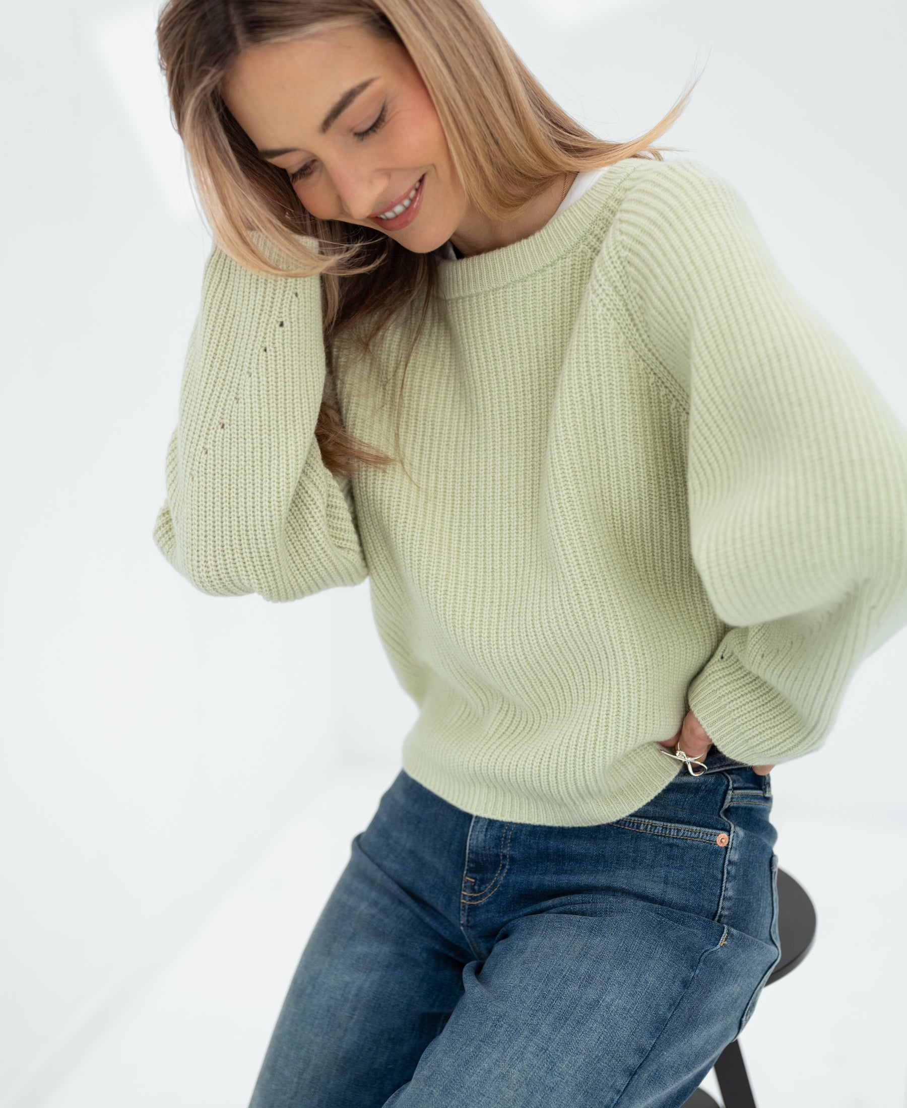 Woman wearing a light green merino wool sweater in a bright room.