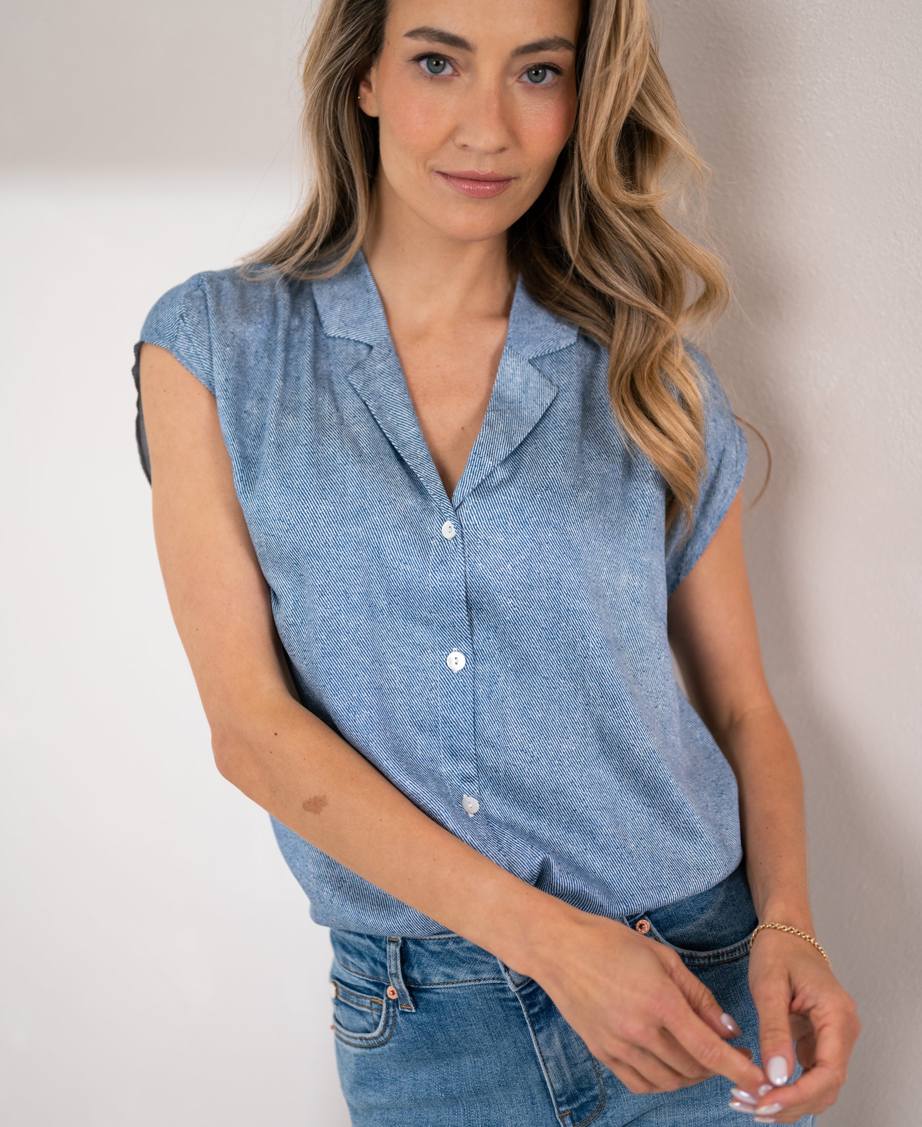 Woman wearing light blue printed blouse by PLEIN PUBLIQUE, shown from the front against a white wall.