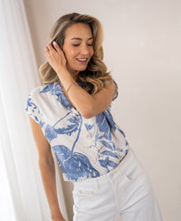 Woman wearing a PLEIN PUBLIQUE LA DILOU floral print blouse, touching her hair in soft light.