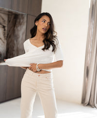 Cream linen T-shirt in a bright room, held out to show its fit and fabric. Natural light highlights the texture.