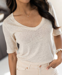 Woman wears cream linen T-shirt indoors.