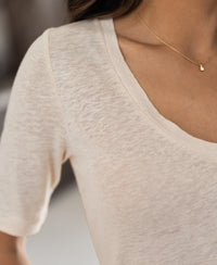 Close-up of a person wearing a cream-colored linen T-shirt from PLEIN PUBLIQUE, LA DOMI style.