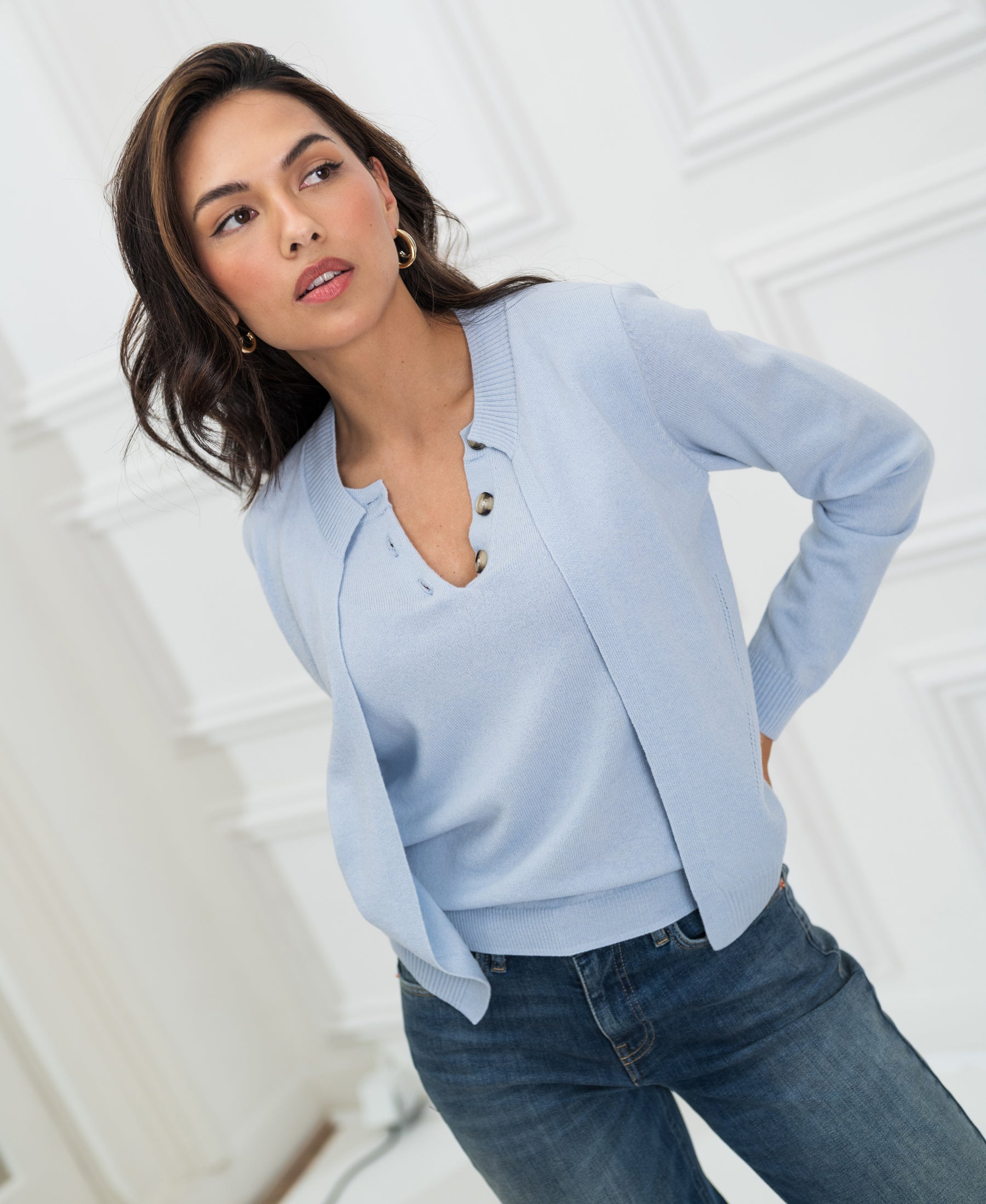 Light blue women's cardigan sweater by Plein Publique shown from the side against a white paneled wall.