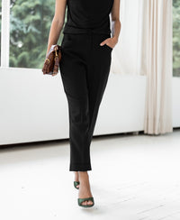 Person wearing PLEIN PUBLIQUE 7/8 LE FAUBOURG black trousers, standing by large windows.