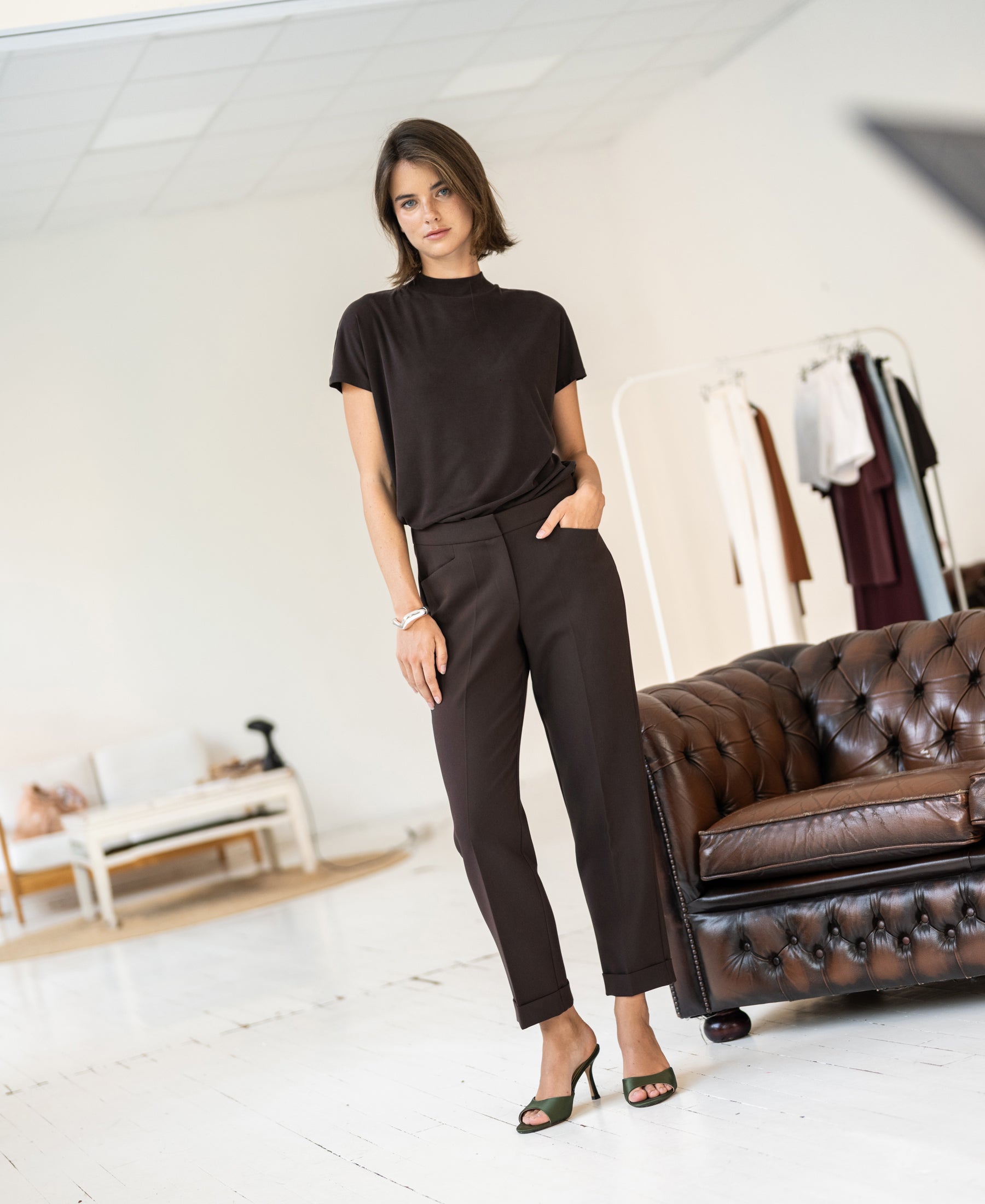 Brown 7/8-length pants in pure chocolate color, shown on a woman standing by a brown leather sofa.