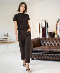 Cropped brown trousers in a stylish room, shown near a brown sofa.