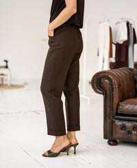 Person wearing brown cropped pants stands by a brown leather sofa.