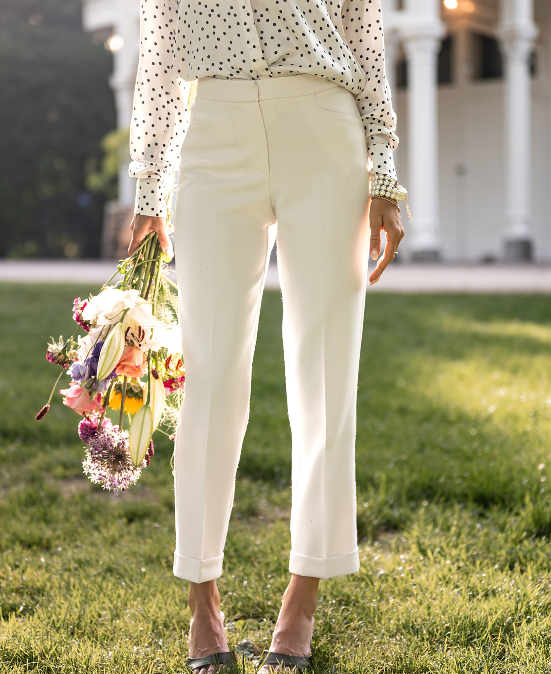 Woman wearing PLEIN PUBLIQUE Tapered Trousers LE FAUBOURG Cream, standing on grass near building.