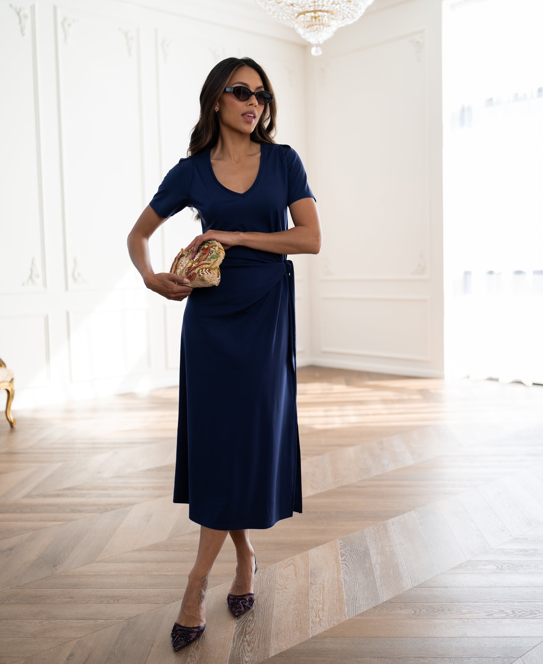 Woman wearing a PLEIN PUBLIQUE long dress LA FILICIA in dark blue stands in an elegant room.