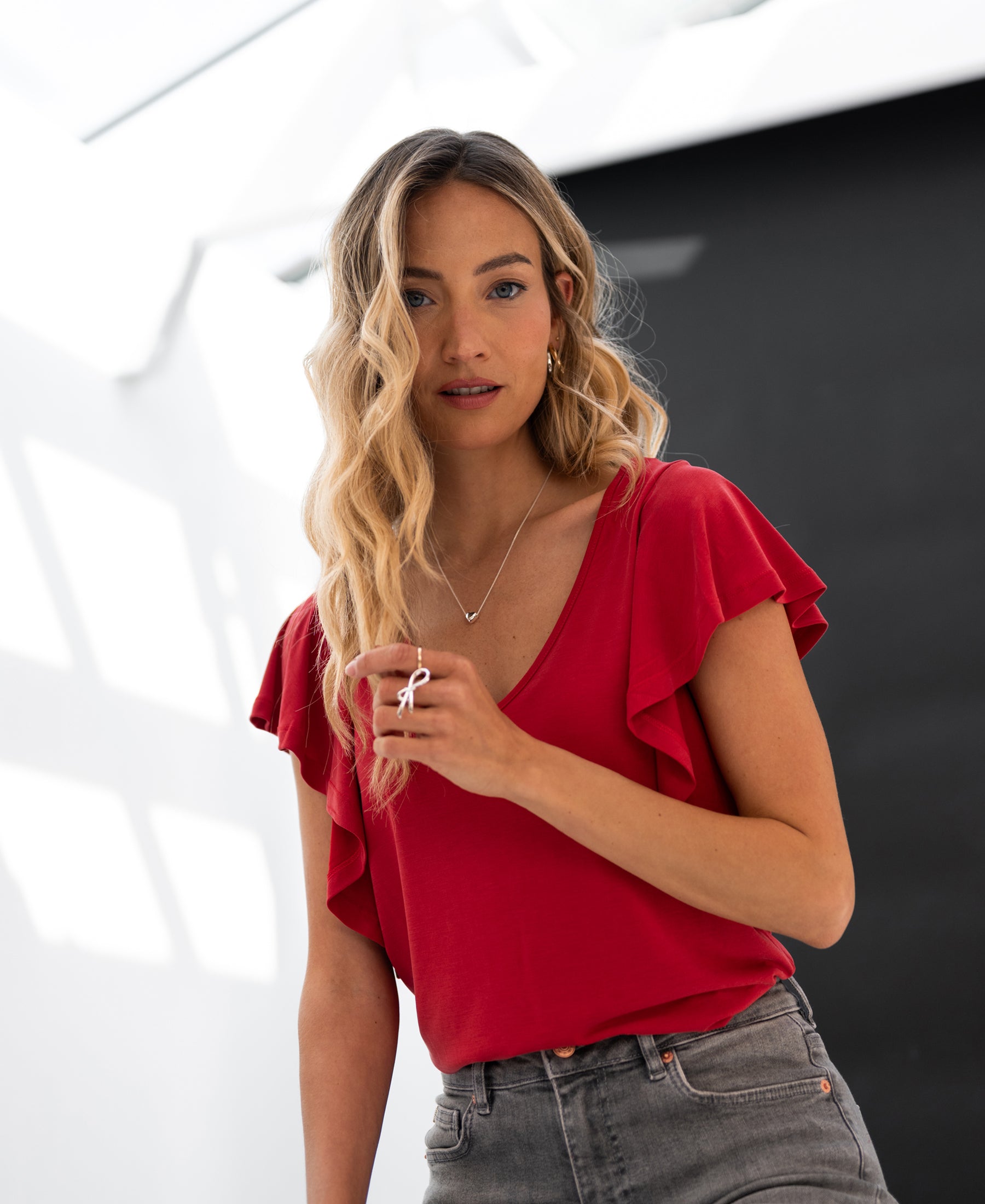 Woman wearing a red PLEIN PUBLIQUE Twoway top poses indoors, holding a necklace.